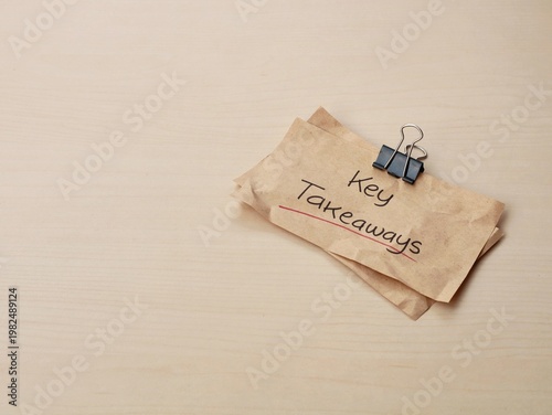 Key takeaways handwritten on brown paper with binder clip on wooden desk. Perfect for business, education, and summary-related concepts