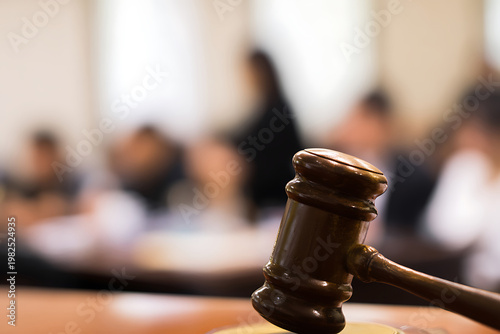 Gavel on a wooden table in a courtroom with blurred people in the background.