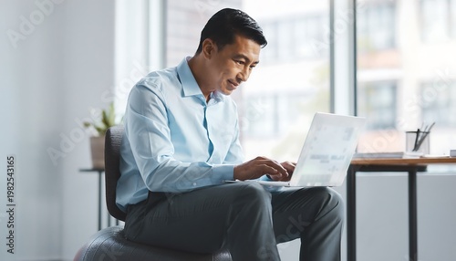 Focused Asian businessman working on laptop in modern office 1.