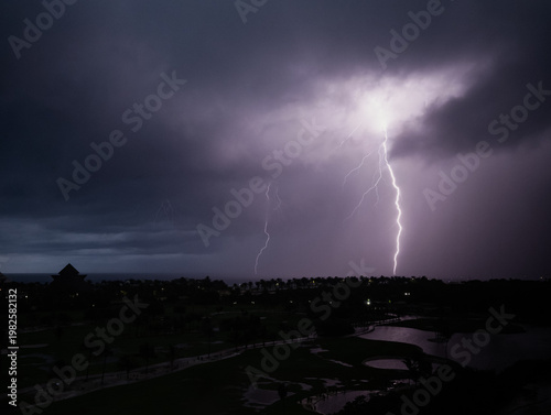 A dramatic lightning bolt illuminates an overcast sky over a golf course, creating a stunning contrast between nature's fury and the tranquil landscape below.
