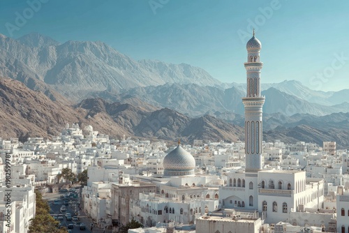 An expansive aerial view showcases a traditional white-walled city nestled against a backdrop of rugged mountains under a clear blue sky, dominated by a prominent mosque with a soaring minaret.
