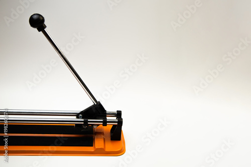 An orange mechanical tile cutter with a metal river lies on a white background on the side with space for text. The concept of renovation, tiling, construction work. High quality photo 