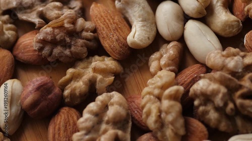 Close-up of whole peeled nuts mix on a wooden background. Appetizing assortment of almonds, cashews, hazelnuts, and walnuts rotating under warm light
