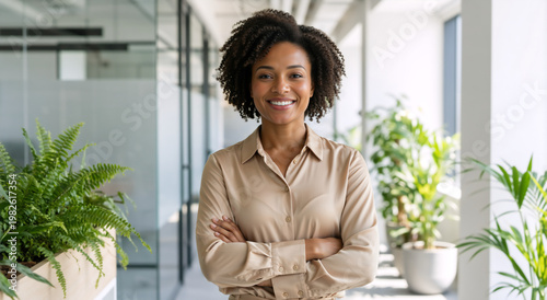 Portrait of smiling confident businesswoman with arms crossed in modern office. Friendly female professional looking at camera