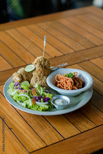 Crispy fried chicken served with spaghetti and fresh salad on plate over wooden table. Clean composition with copy space for text. Casual dining concept.