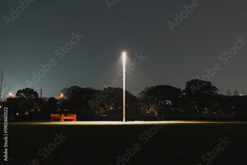 A lonely street lamp casting a solitary pool of light in a nearly jet-black public park at night.