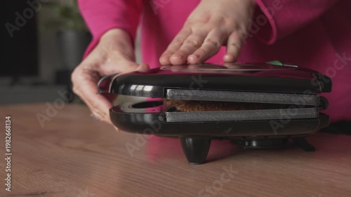 The hands of a housewife woman hold a mini grill in which homemade food and sandwiches are prepared.