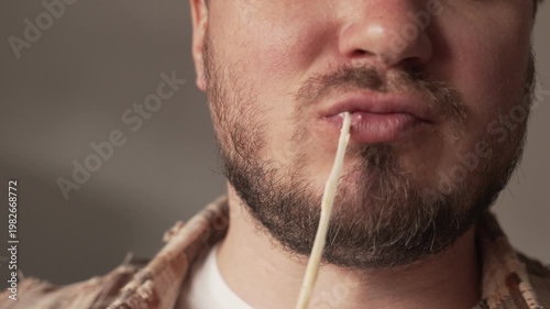 A man takes a close-up bite of a cooked sandwich, from which the melted cheese stretches.