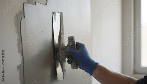 Hands in blue gloves applying plaster to a wall with a metal trowel during construction