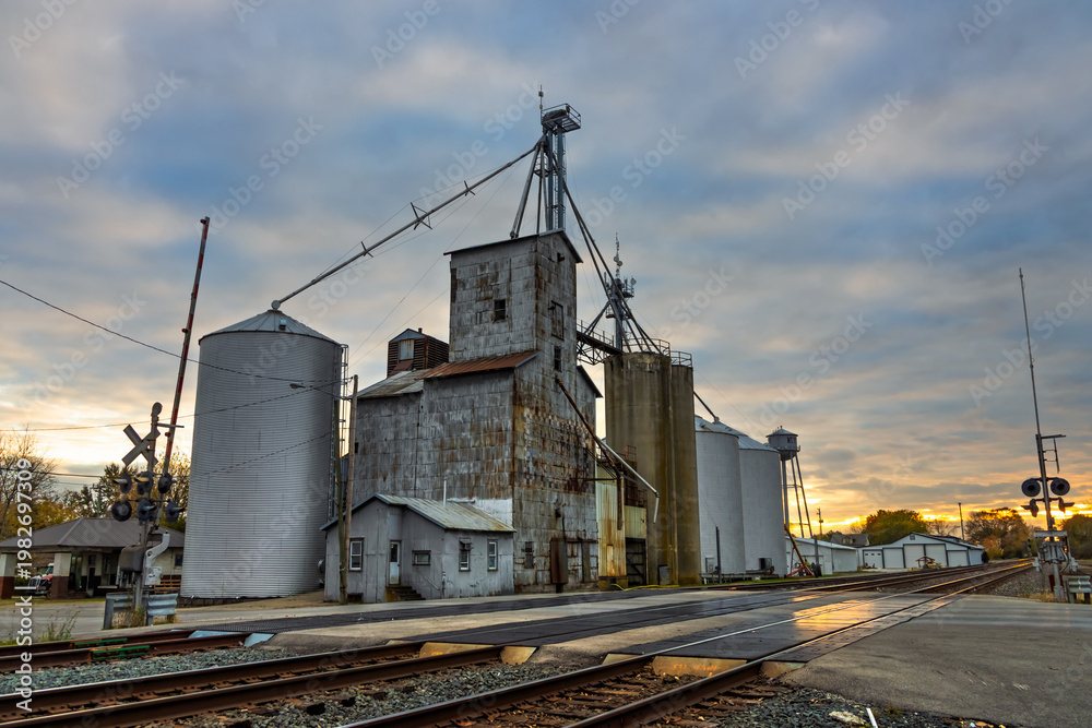 Obraz premium Grain elevators and railroad tracks at sunset in small town