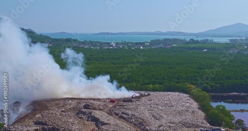 Aerial view of a landfill fire in Phuket with heavy smoke spreading across nearby landscapes and urban areas. Thick plumes of smoke rise illustrating the impact of urban waste and air pollution.