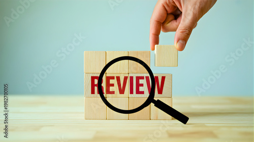 Hand placing block on 'REVIEW' text under magnifying glass, symbolizing ongoing business analysis, strategic evaluation, and continuous improvement