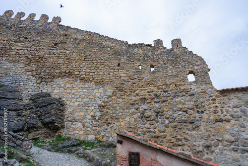 The historic stone walls of the medieval castle in Albarracin, Spain, winding along the rocky hillside with traditional red brick houses below.