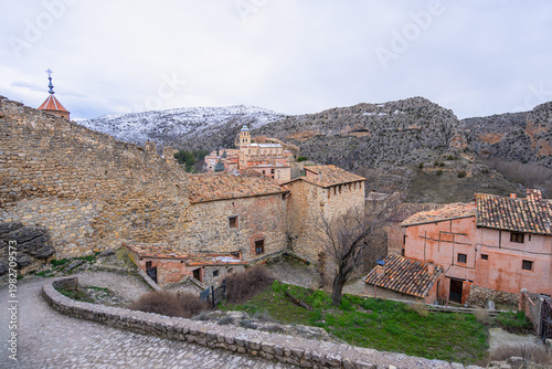 A scenic view of the historic medieval town of Albarracin in Spain, featuring stone buildings, narrow streets, and snow-capped mountains in the background.