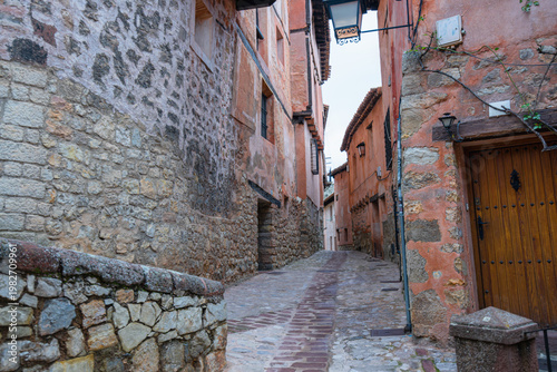 A narrow, cobblestone street lined with historic medieval stone buildings in the picturesque town of Albarracin, Spain.