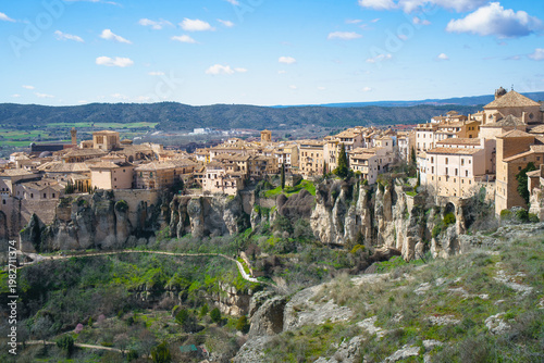A scenic view of the historic city of Cuenca, Spain, featuring ancient buildings perched on dramatic limestone cliffs carved by river erosion.