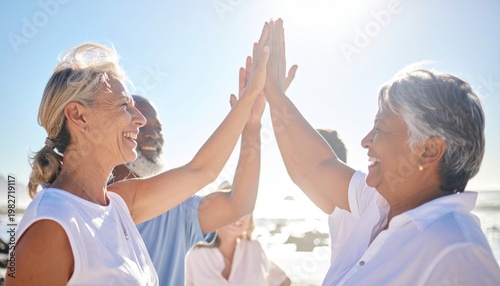 Diverse group of senior friends celebrating success with high fives on a sunny beach.