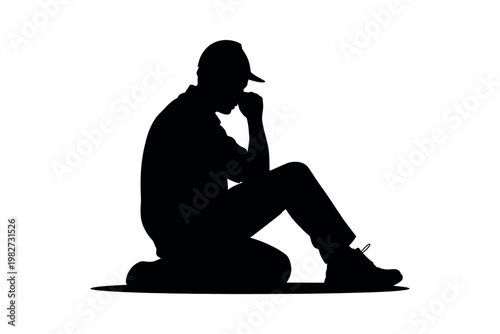 A silhouette of a man sitting alone in deep thought on the ground with his hand on his chin