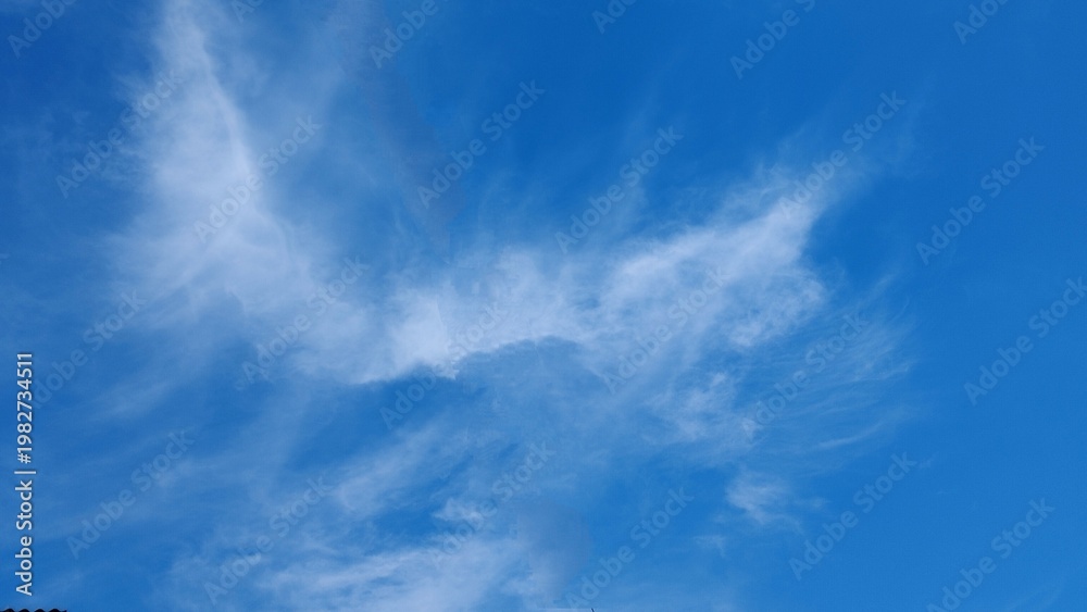 Obraz premium Fluffy white clouds drift across a bright blue nature sky as golden sun light illuminates a summer day atmosphere