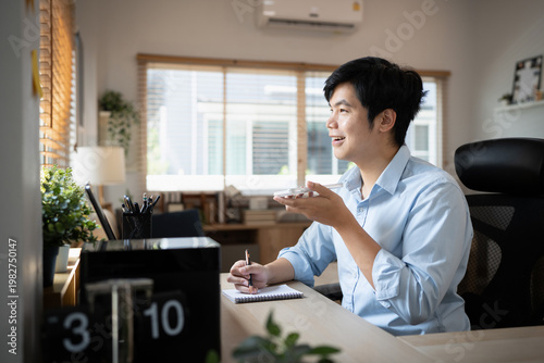 Smiling businessman talking on mobile phone while taking notes at modern home office desk