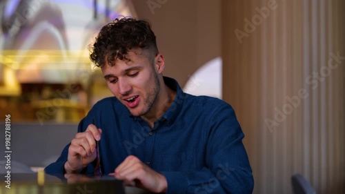 Close up of happy young man sitting in cafe indoor and eating wok food. Curly handsome Caucasian guy in modern restaurant having tasty meal. Delicious healthy food. Nutrition. Real time.