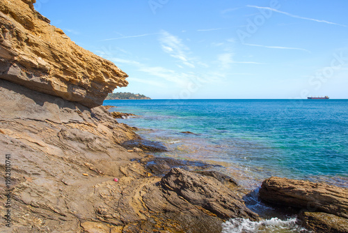 Picturesque rocky coastline of Mediterranean sea. Tanker ship on the horizon
