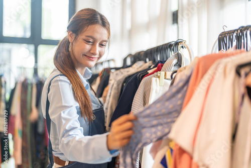 Happy female small business owner in denim apron checking clothing rack in fashion boutique, Retail store manager arranging apparel inventory, SME entrepreneur lifestyle and shop management concept