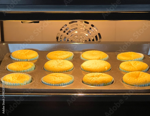 Freshly baked homemade muffins in paper cups on baking tray inside modern oven, golden cupcakes rising during baking process in kitchen. baking in a home oven. easy cooking