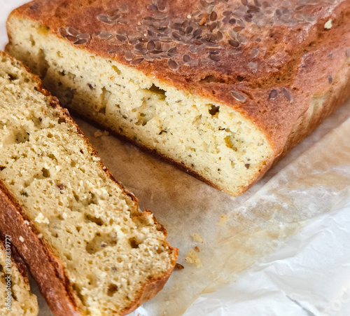 Freshly baked keto bread loaf with flax seeds on top, sliced and resting on parchment paper.