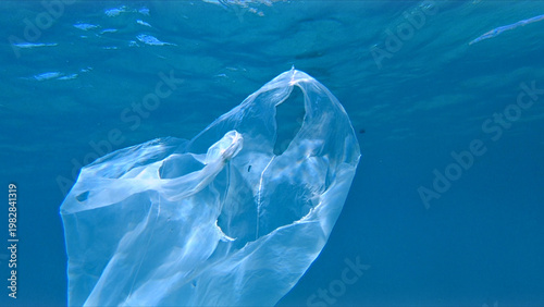 Fotografija A large transparent plastic bag floats in clear blue water, highlighting environmental damage