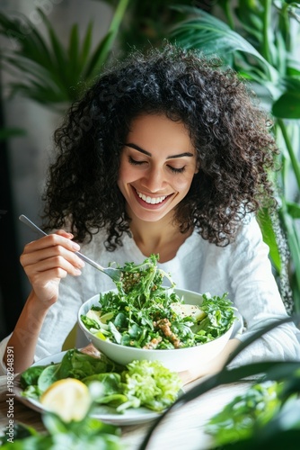 Happy woman enjoys a healthy salad at the table with fresh ingredients in a bright green indoor space