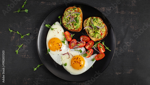 Healthy breakfast with avocado toast and fried eggs  on dark background. Top view