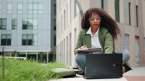 Modern business woman working on laptop sitting outdoors office building