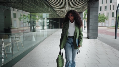 Smiling African American female in trendy blazer walking with determination. Modern businesswoman employee looking to camera in the office