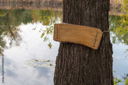 Empty wooden sign on a tree against pond in a park