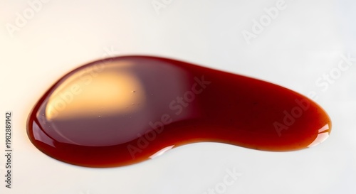 Close up of a dark liquid droplet on a light surface with soft lighting