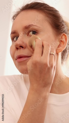 Young woman applying foundation with beauty sponge on face during makeup routine at home. Perfect for beauty, cosmetics, skincare, makeup tutorial and lifestyle themed projects