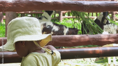 Adorable cute toddler girl feeding little goats and sheeps on a kids farm. Beautiful baby child petting animals in the zoo. Excited and happy girl on family weekend.