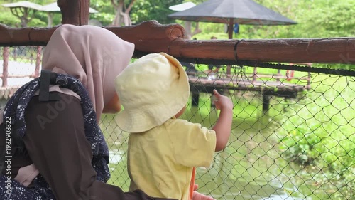 Woman at a zoo with child, observing animals behind a fence. Perfect for illustrating family outings, wildlife conservation, and education.
