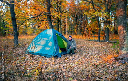 elderly man Tourist sits near a tent in the forest at sunset