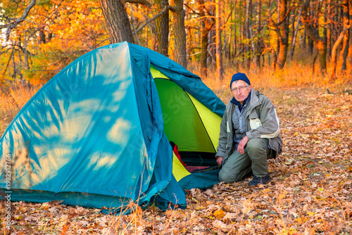 elderly man Tourist sits near a tent in the forest at sunset