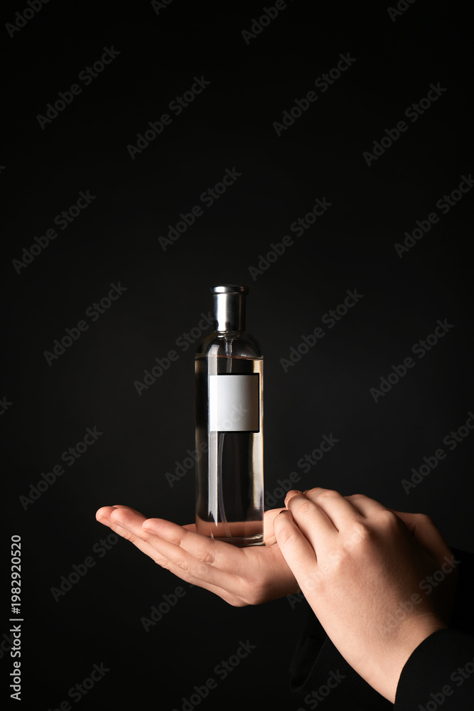 Naklejka premium Female hands with bottle of perfume on black background