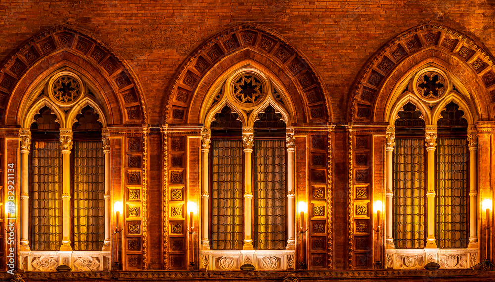 Obraz premium old yellow facade of house with three brown vintage windows in retro gothic italian european style. Night italian architecture.