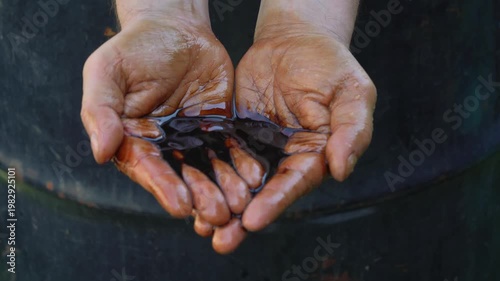 Close up of oil worker hands hold oil in palms on background of barrel. Oil industry, production, petroleum production. Fuel