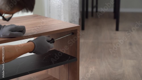 Furniture assembler assembles wooden nightstand using screwdriver. Process of assembling furniture
