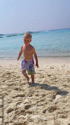 A child walks along a sandy beach by the clear water, enjoying a sunny day by the sea.
