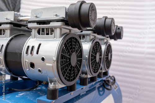 Rear view of a portable oil-free air compressor with a blue horizontal receiver tank, twin-cylinder motor unit, and rubber-coated transport wheels