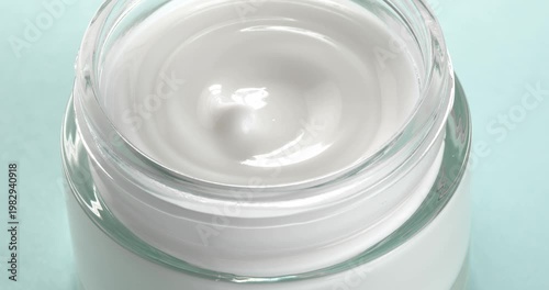 Open jar with cosmetic facial cream on blue background close-up on a rotating table.