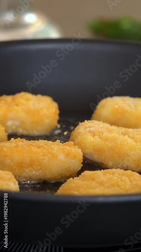 Camera movement on fried chicken nuggets in hot oil in frying pan. Nuggets fry with crispy crust. Food. Vertical shot