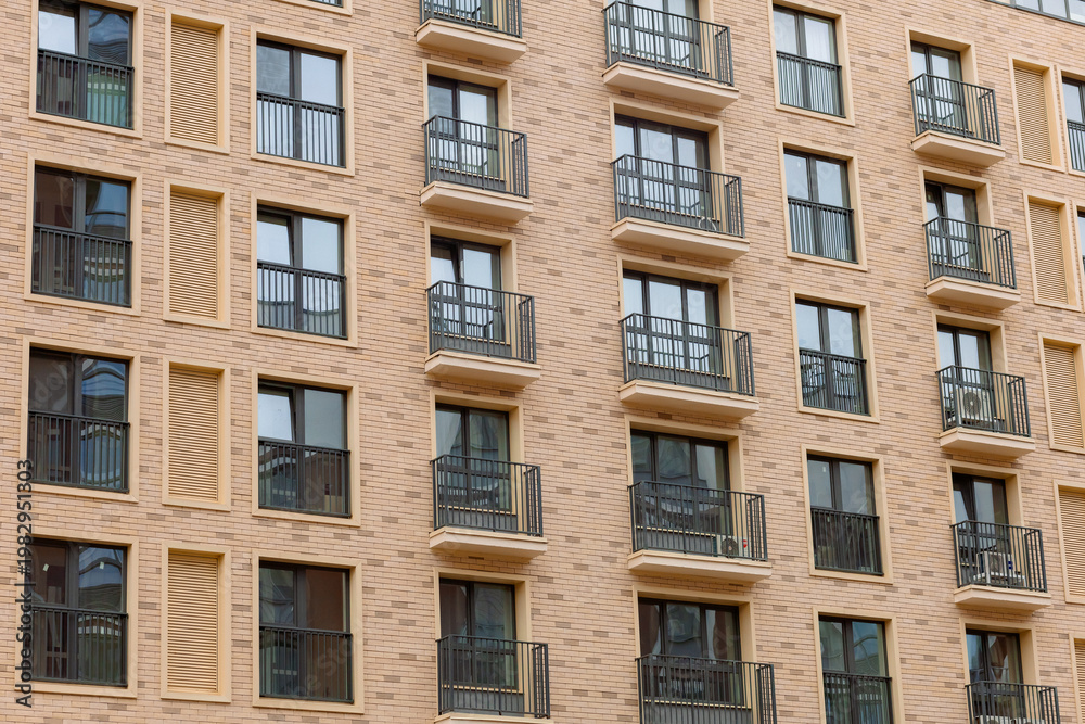 Fototapeta premium Modern apartment building with curved, textured facade. Balconies feature black railings and glass doors. Warm beige tones contrast with dark window frames